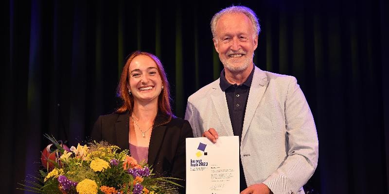 Hannah J. Kohler zusammen mit OB a.D. Roland Klenk mit Urkunde und Blumenstrauß bei der kunsthub 2023-Preisverleihung