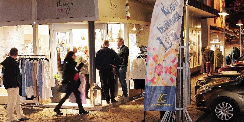 Menschen stehen abends vor einem Modegeschäft, betrachten Kleidung und unterhalten sich auf der Straße