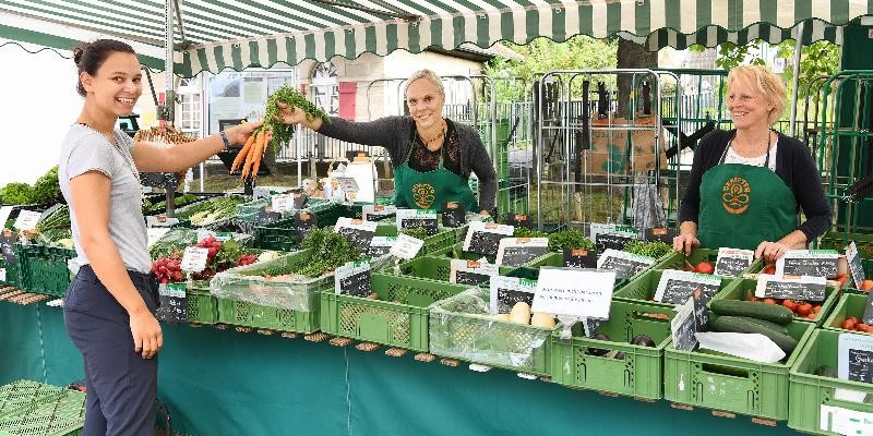 Gemüsetand mit Verkäuferin und Kunden auf einem Wochenmarkt