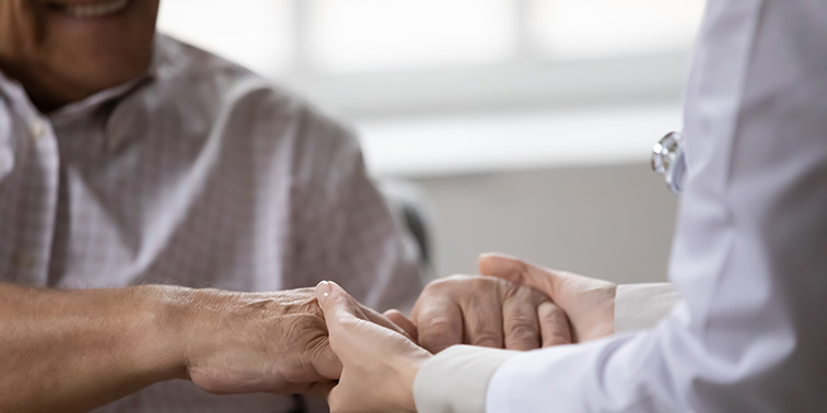Ein Arzt hält die Hand eines älteren Mannes in einem fürsorglichen Moment.