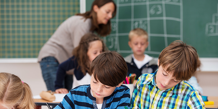 Lehrerin hilft Grundschulkindern im Klassenraum beim Arbeiten an ihren Aufgaben.