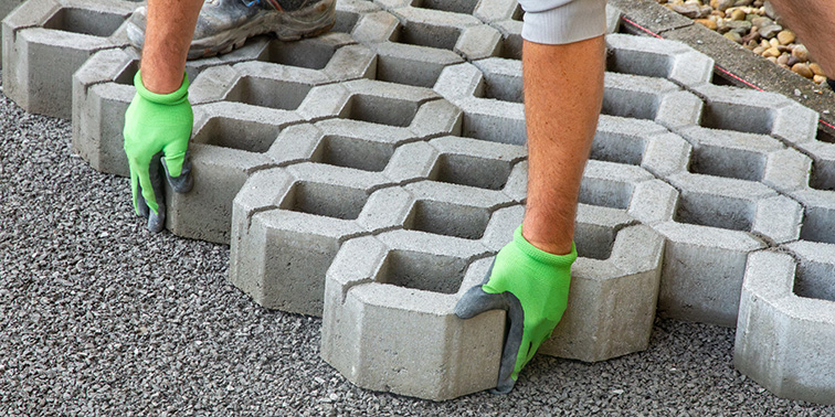Handwerker verlegt Pflastersteine mit grünen Schutzhandschuhen