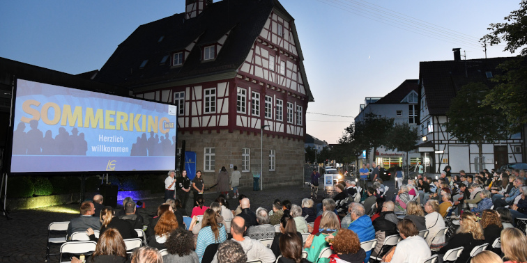 Open-Air-Kinoabend in Echterdingen: viele Menschen sitzen vor Leinwand mit ‚Sommerkino‘-Schriftzug, Fachwerkhaus im Hintergrund.