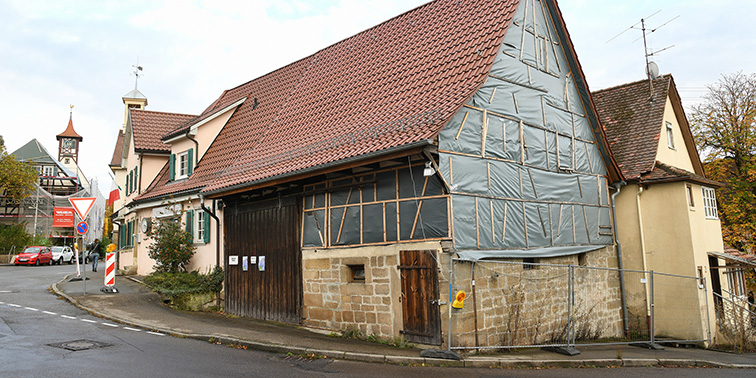 Ein Fachwerkhaus an einer Straßenecke, teilweise eingerüstet und mit Bauzaun abgesperrt, daneben weitere historische Gebäude.