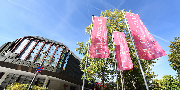 Filderhalle Convention & Event Center mit pinken Fahnen vor modernem Gebäude und blauem Himmel.