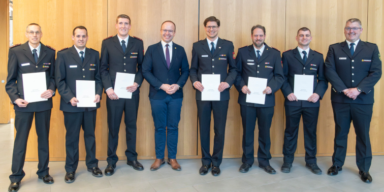 Mehrere Feuerwehrmänner in Uniform stehen nebeneinander und halten Urkunden bei einer Ehrung.