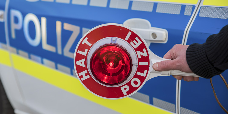 Kelle "Halt Polizei" vor Teil eines Streifenwagens der Polizei