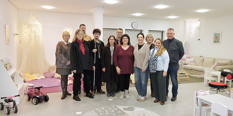Eine Gruppe von Erwachsenen steht in einem freundlich eingerichteten Kinderraum für ein gemeinsames Foto zusammen.