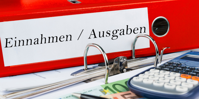 Roter Dokumentenordner mit der Aufschrift "Einnahmen/Ausgaben" und ein Taschenrechner