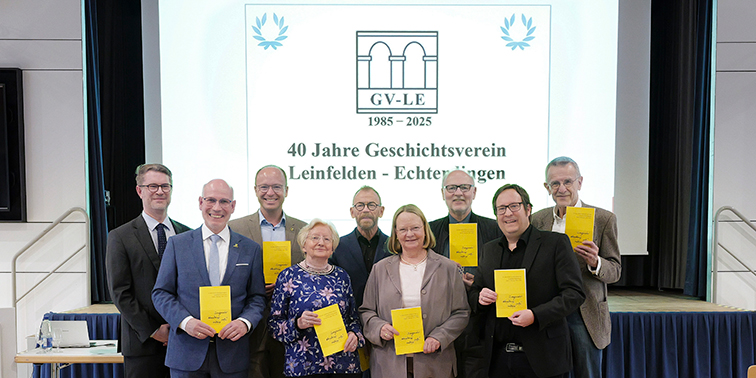 Gruppenfoto von neun Personen auf einer Bühne mit einem gelben Heft in der Hand, aufgenommen anlässlich des 40-jährigen Jubiläums des Geschichtsvereins Leinfelden-Echterdingen (1985–2025). Im Hintergrund ist ein Logo und der Schriftzug der Veranstaltung zu sehen.