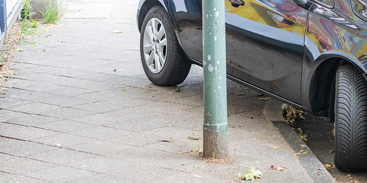 Foto: Ein schwarzes Auto steht am Straßenrand (zum Teil auf dem Gehweg) geparkt.
