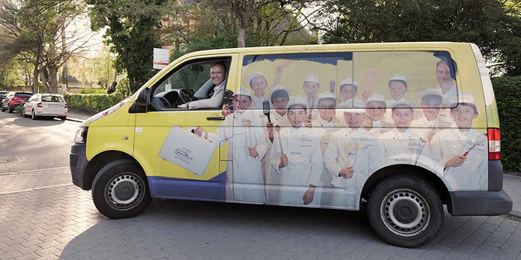 Ein gelbes Kultur-Shuttle mit großem Aufdruck fährt auf einer Straße; am Steuer sitzt ein Oberbürgermeister Otto Ruppaner, auf den Fahrzeugseiten sind mehrere abgebildete Personen zu sehen.