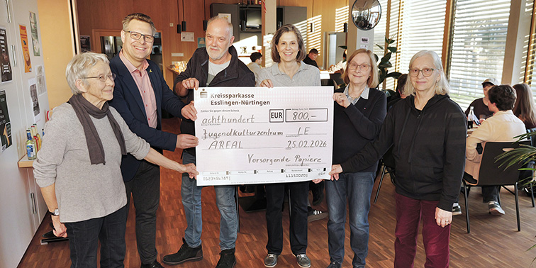 Eine Gruppe von Personen hält einen großen symbolischen Scheck in einem Raum und lächelt in die Kamera.