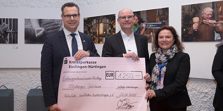 Drei Personen halten einen symbolischen Scheck über 1.250 Euro für das 50-jährige Jubiläum des Fotoclubs Leinfelden-Echterdingen e.V. im Ausstellungsraum.