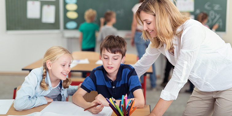 Lehrerin unterstützt zwei Kinder beim gemeinsamen Lernen im Klassenzimmer.