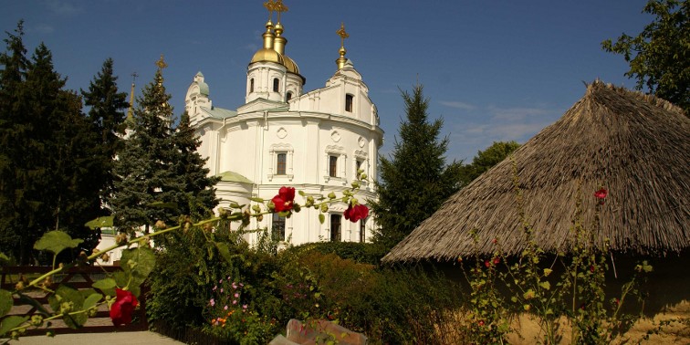 Weiße Kirche mit goldfarbenen Dachkuppeln (umgeben von grünen Bäumen) im ukrainischen Poltawa
