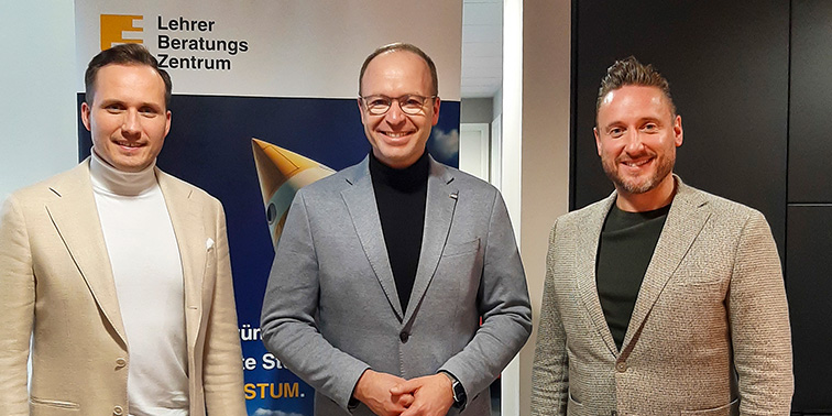 Drei Personen stehen in einem Innenraum vor einem Banner und posieren für ein Foto.