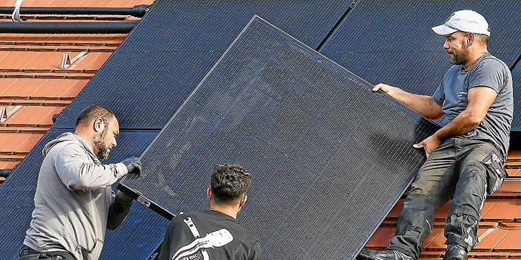 Drei Männer installieren ein Solarpanel auf einem Hausdach.