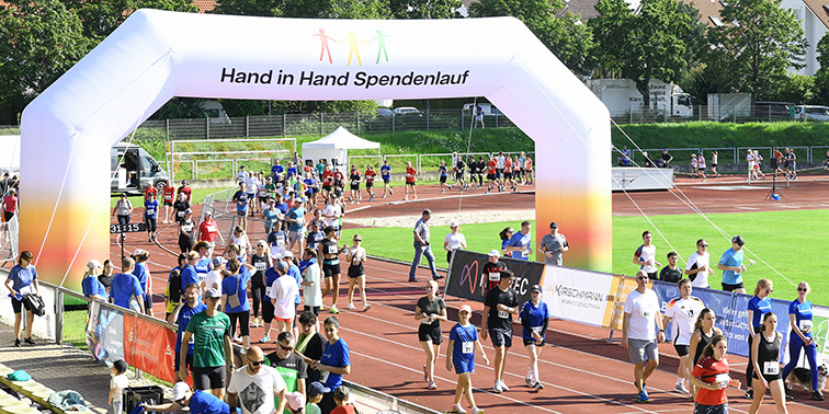 Viele Teilnehmer eines Spendenlaufs auf einer Laufbahn unter einem großen Torbogen mit der Aufschrift „Hand in Hand Spendenlauf“