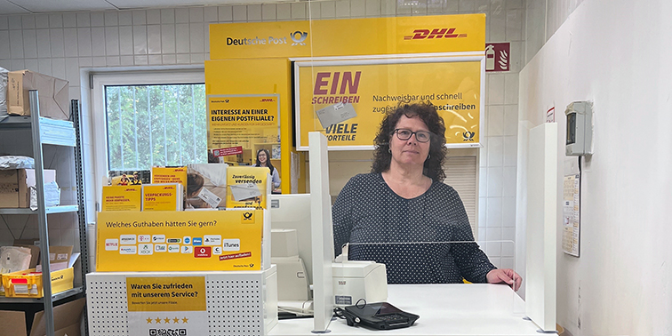 Eine Mitarbeiterin steht hinter dem Schalter einer Postfiliale.