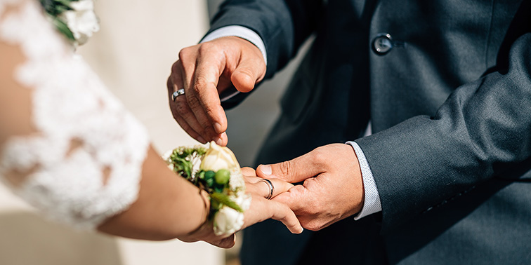 Ein Paar steckt sich während einer Hochzeit feierlich die Ringe an.
