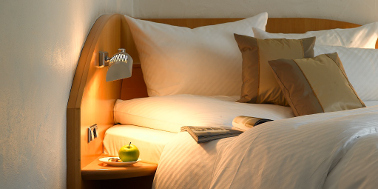 Hotelzimmer mit Bett aus hellem Holz und weißen Oberbett 