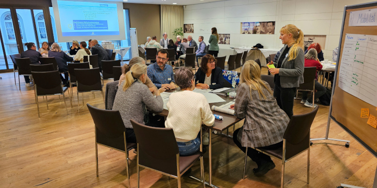 Personengrupppen sitzen an drei Tischen in verschiedenen Arbeitsgruppen