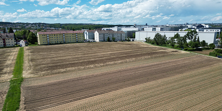 Ackerfläche mit angrenzender Wohn- und Gewerbebebauung unter blauem Himmel