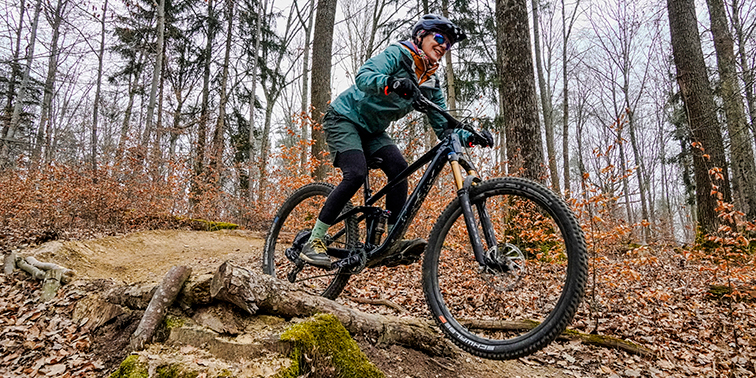 Eine Mountainbikerin fährt mit ihrem Fahrrad über eine Wurzel auf einem Waldweg.