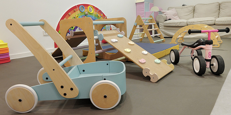 Indoor-Spielbereich mit Holzspielzeug, kleiner Rutsche und Dreirad vor einem Sofa.