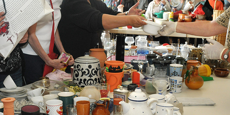 Nachhaltig tauschen: Warentauschtag am 14. März Eine Gruppe von Menschen steht um einen Tisch, der mit unterschiedlichen Gegenständen und Materialien gefüllt ist.