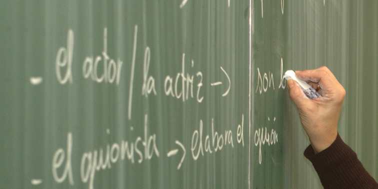 Lehrerin schreibt spanische Vokabeln mit Kreide an eine Schultafel.