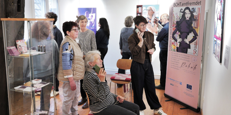Besucher betrachten Kunstwerke in einer Ausstellung, einige sprechen, andere fotografieren Bilder.
