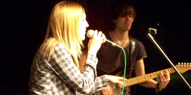 Blonde Sängerin links und E-Girarrist hinten rechts